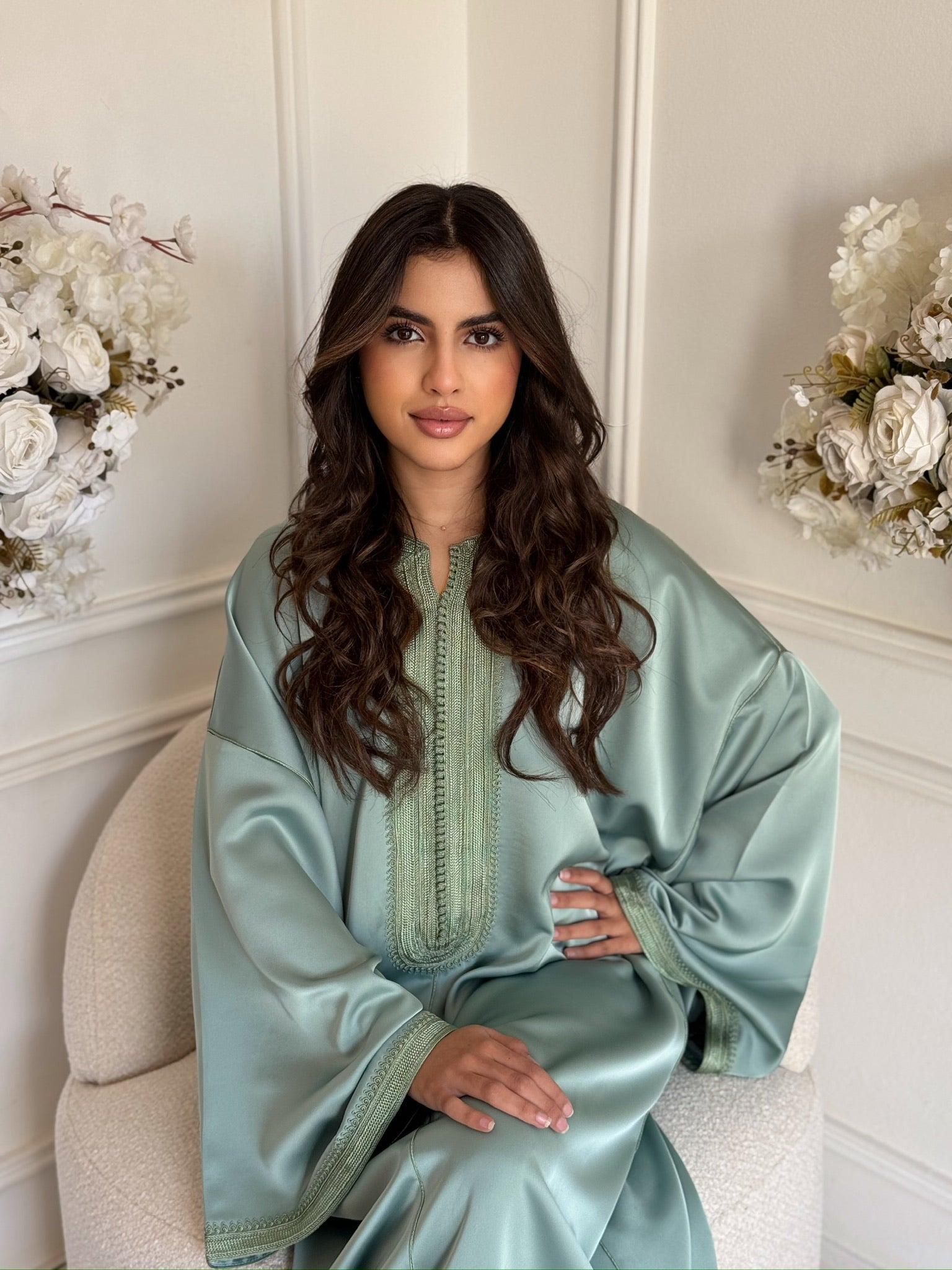 Model wearing a sage green Moroccan gandoura sitting with white floral décor indoors