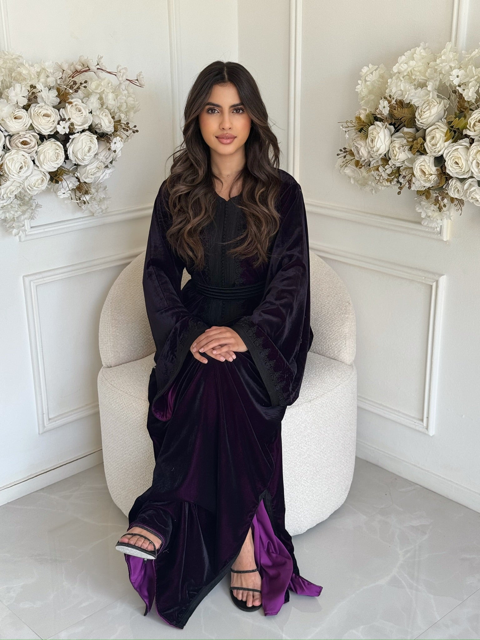 Full view of deep-purple Moroccan caftan in a white room with flowers